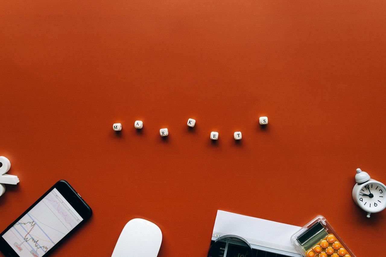 Mastering the First Impression: Your intriguing post title goes here Creative still life with financial tools and the word 'MARKETS' on an orange background.